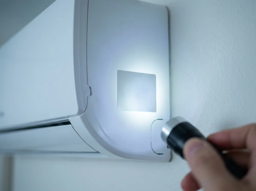 エアコン室内機の側面に貼られた型式表示ラベルを、懐中電灯で照らして確かめている手元